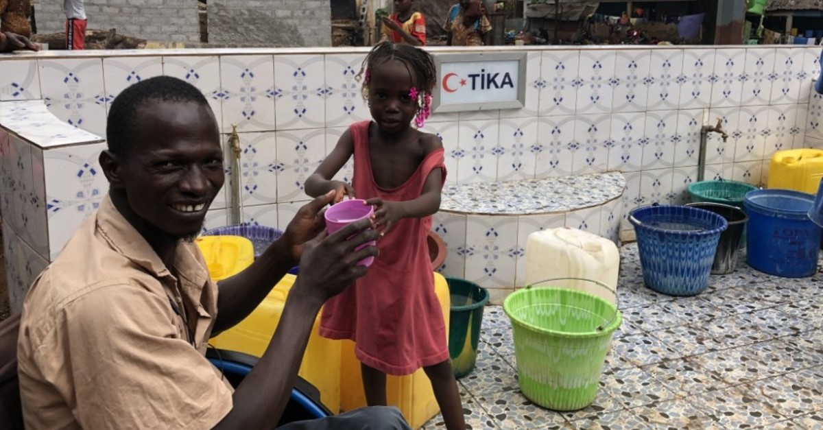 A man helps a girl drink water from a fountain set up by Tu0130KA in Guinea's Conakry where the locals had to walk for kilometers to reach drinkable water.