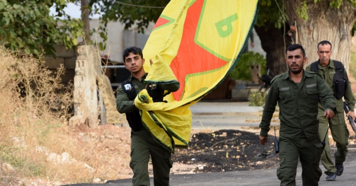 YPG terrorists walk carrying a People's Protection Units (YPG) yellow flag in the Syrian town of Ain al-Arab, along the border with Turkey in the north of Aleppo governorate on Ocotber 18, 2019. (AFP Photo)