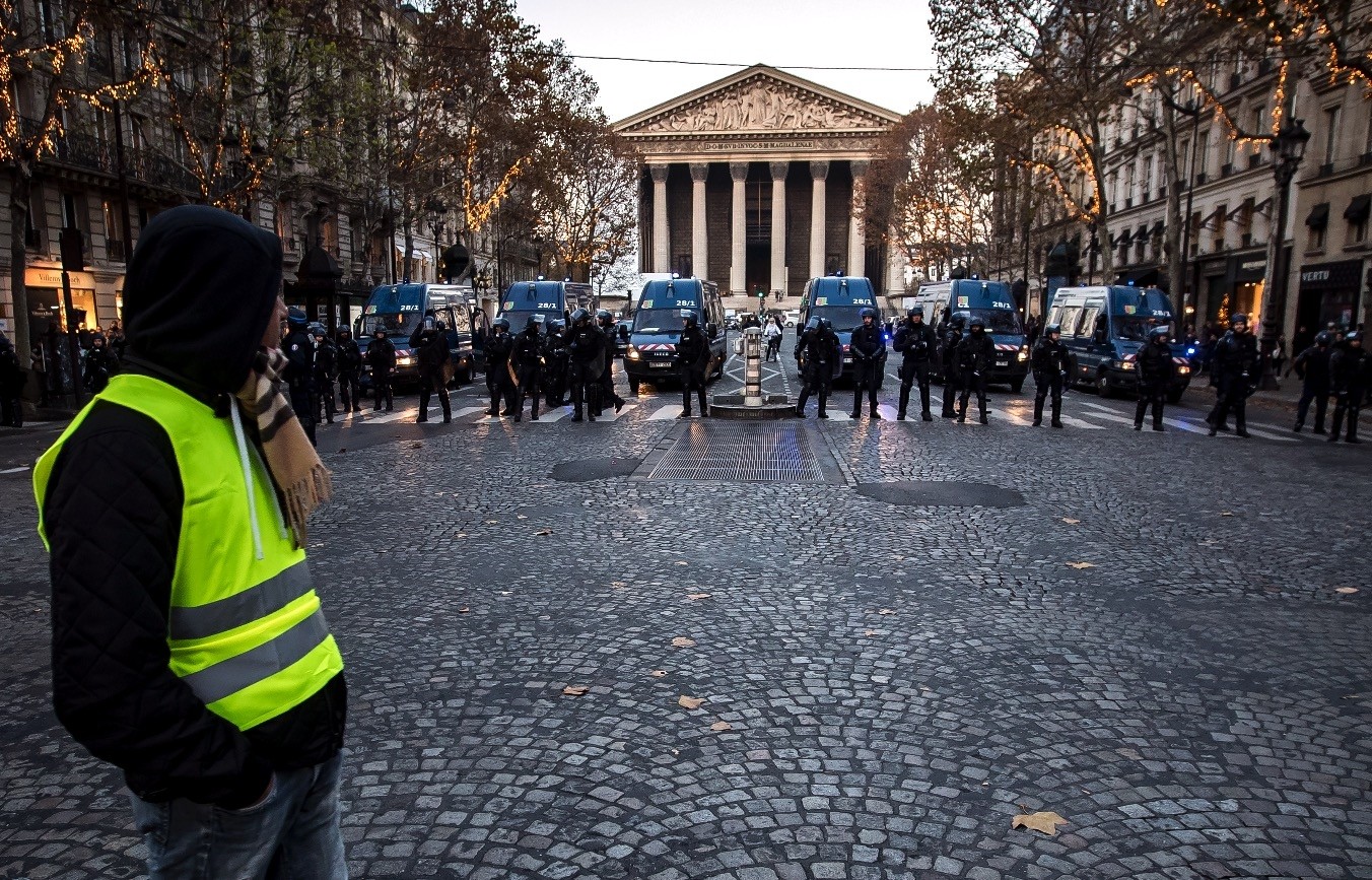 A protesters wearing a yellow vest watches anti-riot police Paris, Nov. 17.