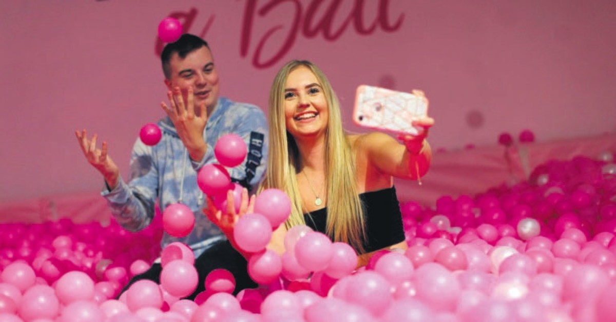Young people pose in a bath of pink balls at The Selfie Factory.