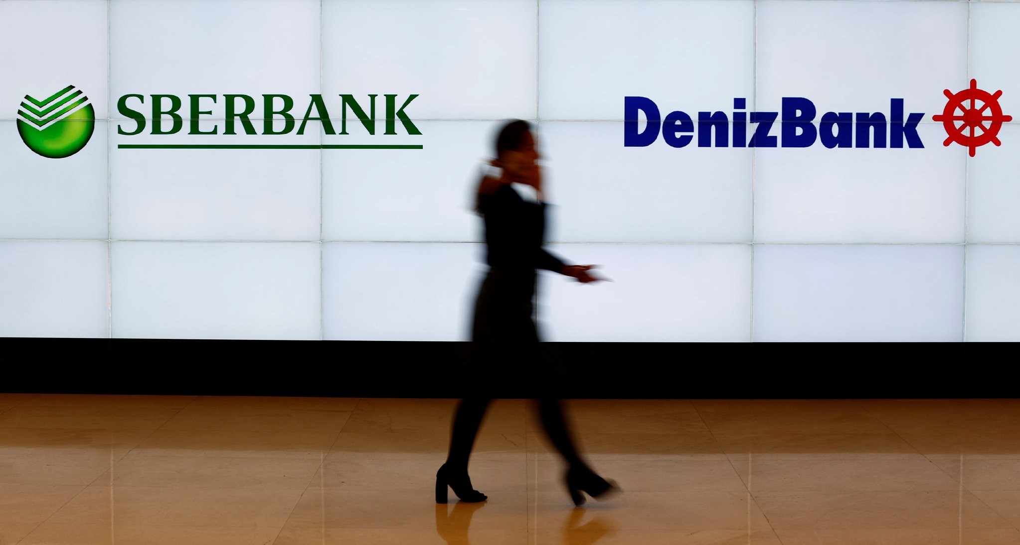 Woman walks past logos of Russiau2019s Sberbank and Turkeyu2019s Denizbank at Denizbanku2019s headquarters in Istanbul, March 2, 2016.