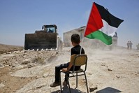 A Palestinian boy sits on a chair with a national flag as Israeli authorities demolish a school site in the village of Yatta, south of the West Bank city of Hebron, July 11.