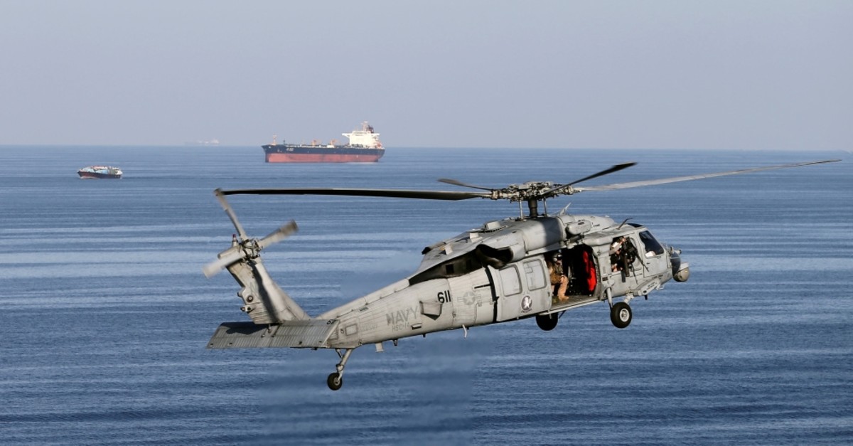 A MH-60S helicopter hovers in the air with an oil tanker in the background as the USS John C. Stennis makes its way to the Gulf through the Strait of Hormuz, Dec. 21, 2018.