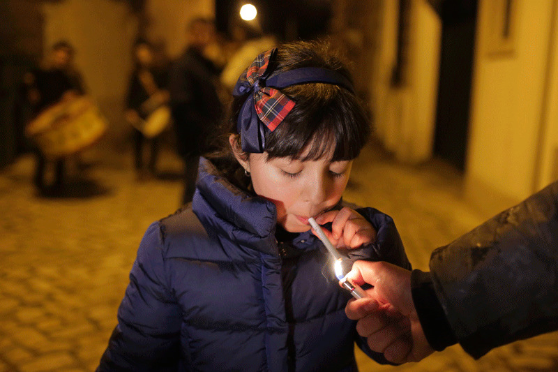 An adult helps a young girl light a cigarette as a band plays in the background in the village of Vale de Salgueiro, northern Portugal, during the local Kings' Feast (AP Photo)