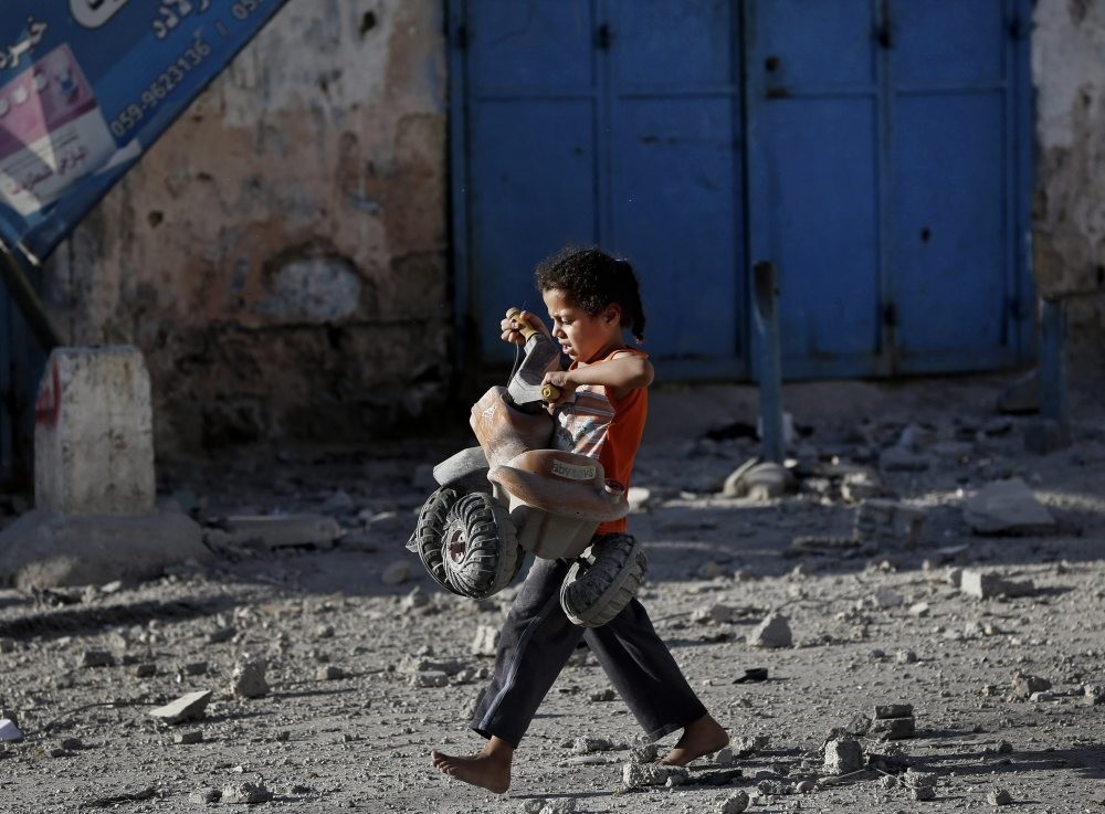 A Palestinian girl walks with a toy that she salvaged from the debris of a building, Gaza City, July 17, 2014.