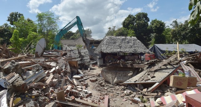 Workers take down a damaged shop with an excavator in an earthquake-hit area in Gangga on August 12, 2018. (AFP Photo)