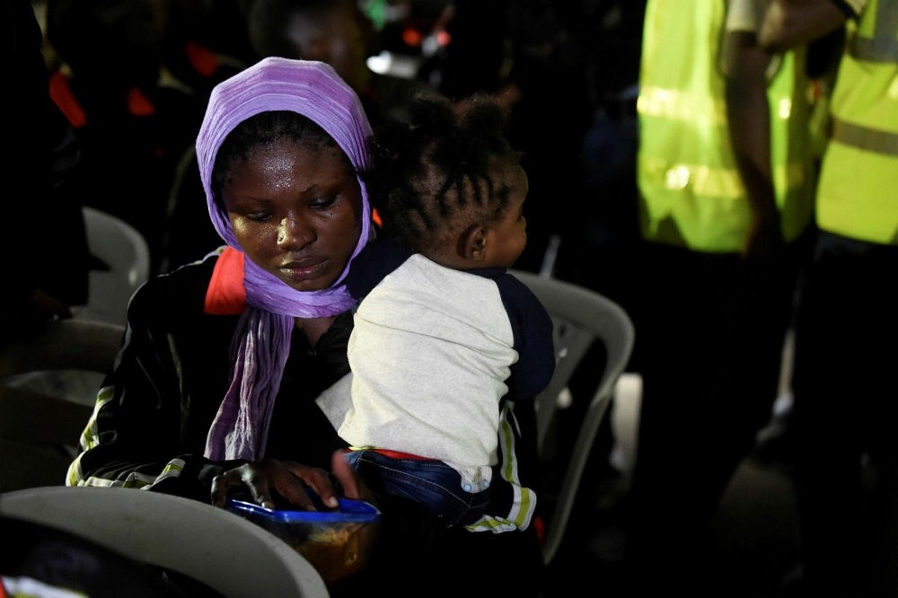 A female migrant tries to feed a child after leaving a chartered aircraft that brought migrants home from Libya, Lagos, Dec. 5, 2017.