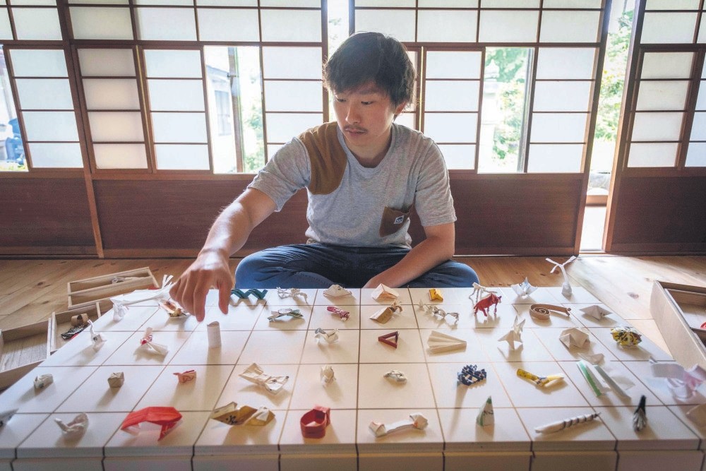 Yuki Tatsumi sits next to his collection of origami made from chopstick sleeves.