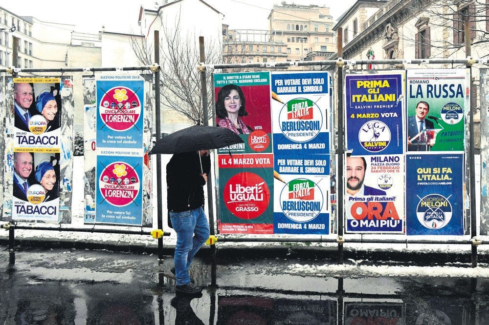A pedestrian passes in front of election posters prior to the Italian elections, Milan, March 1. 