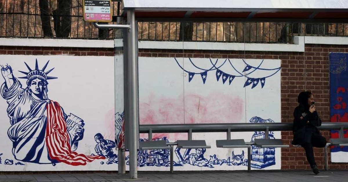 A woman sits at a bus stop in front of an anti-U.S. mural on the former U.S. embassy's wall in Tehran, Iran, Jan. 3, 2020. (Reuters Photo)
