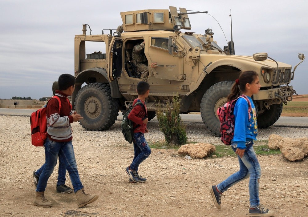 Syrian schoolchildren walk by as U.S. troops patrol an area near the Turkish border in Hasakah, Syria, Nov. 4, 2018.