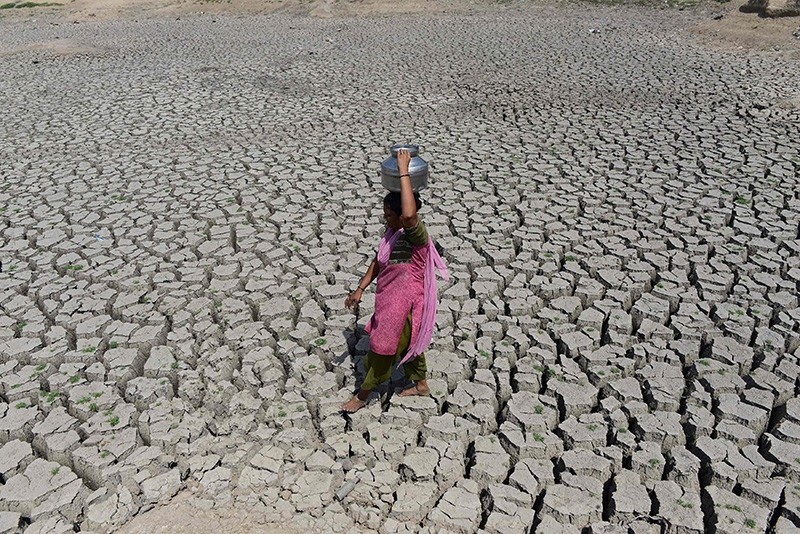 This file photo taken on May 20, 2016 shows an Indian woman walking on the parched bed of Chandola Lake with a metal pot on her head to fetch water in Ahmedabad. (AFP Photo)