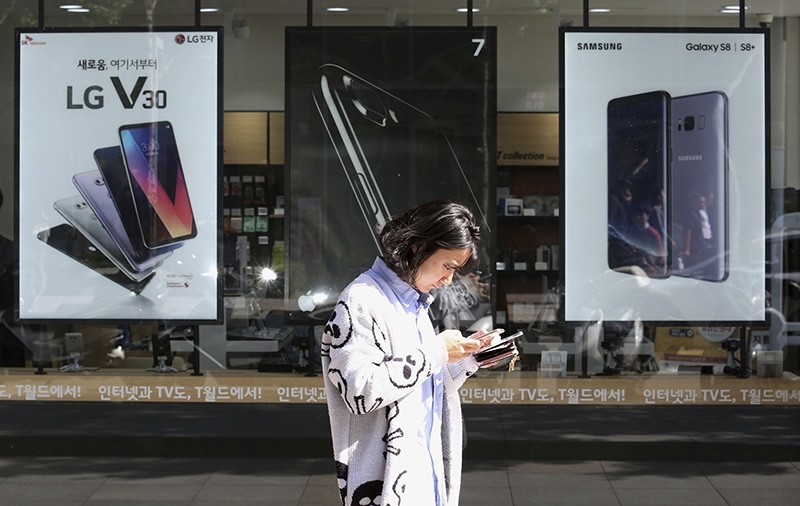 In this Tuesday, Oct. 17, 2017 file photo, a woman walks by posters adverting smartphones at a mobile phone shop in Seoul, South Korea. (AP Photo)
