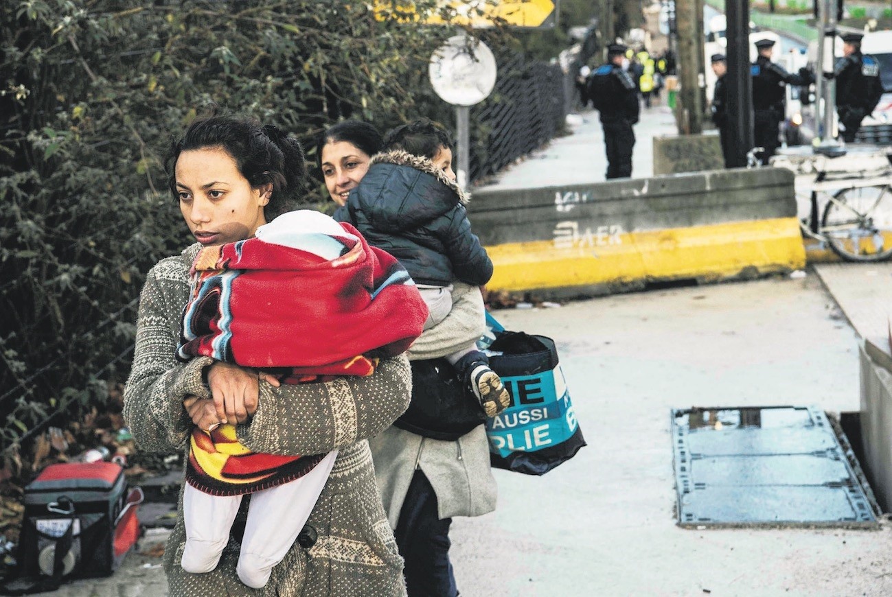 Roma women carry children during their evacuation by police from a makeshift camp, Paris, Nov. 28.