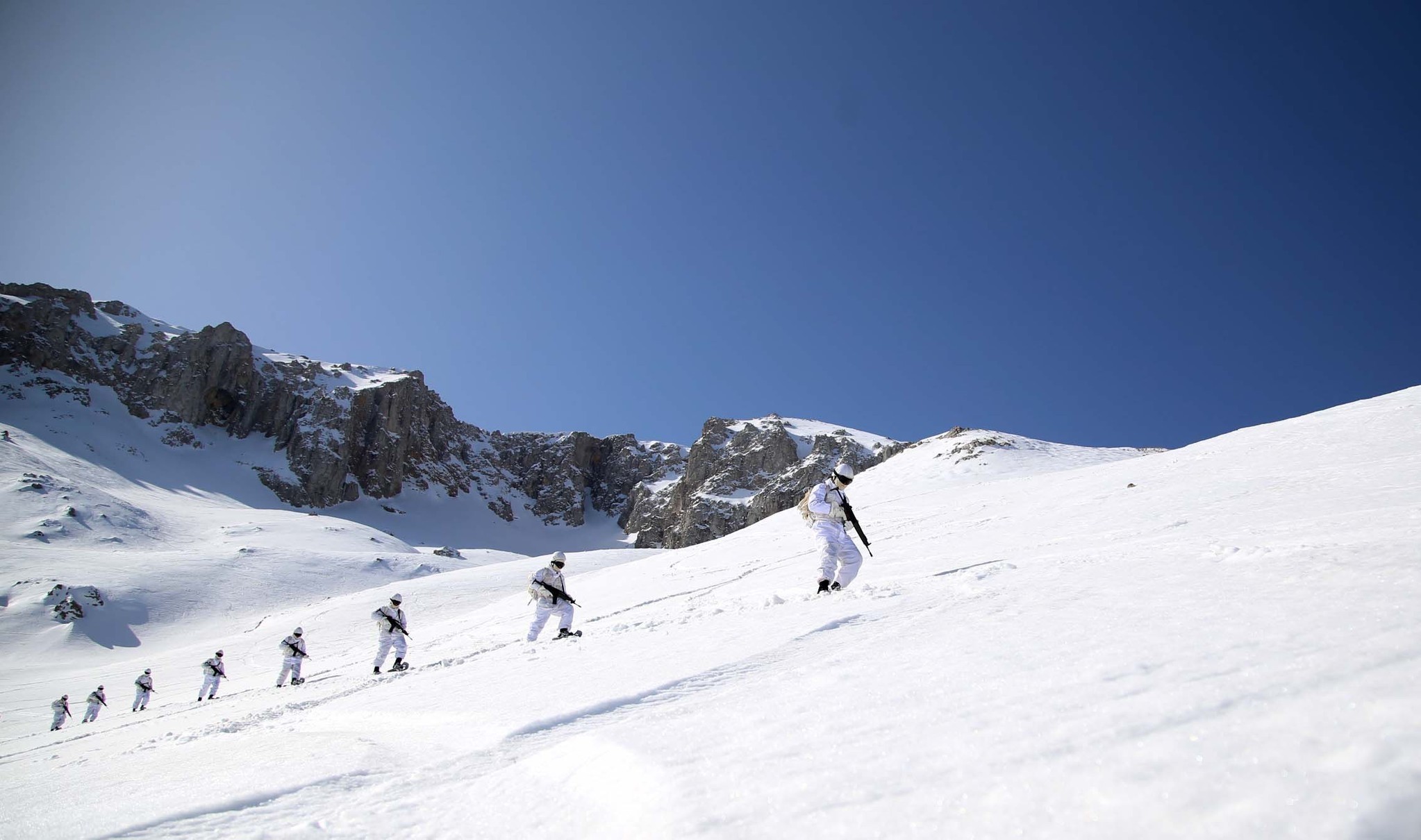 Prospective commandos walk in single file on a snowy slope.