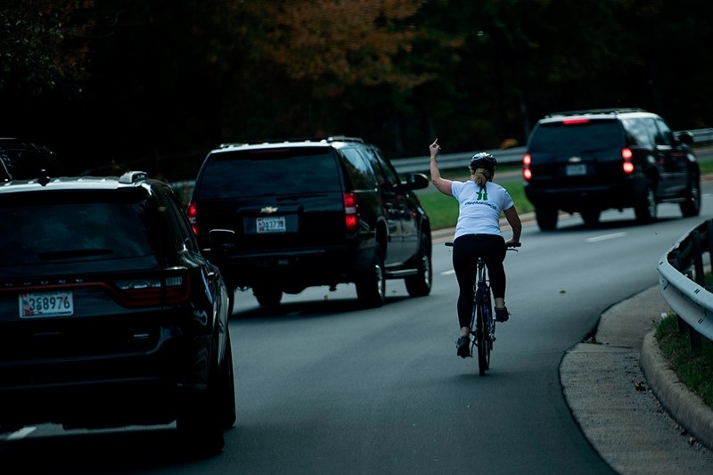 This file photo taken on October 28, 2017 shows a woman on a bike gestures with her middle finger as a motorcade with U.S. President Donald Trump departs Trump National Golf Course in Sterling, Va. (AFP Photo)