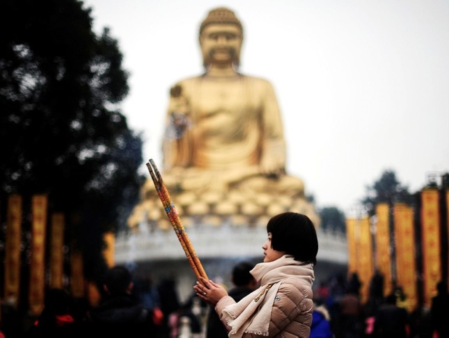 A worshipper offers prayer in front of a Buddha statue for her first visit of the year in Huayan Temple in southwest China. (AP Photo)