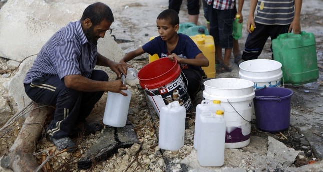 رجل فلسطيني وأطفال يملأون صهاريج بالمياه من محطة رئيسية معطلة في حي الشجاعية في مدينة غزة ، 6 أغسطس / آب 2014 ،