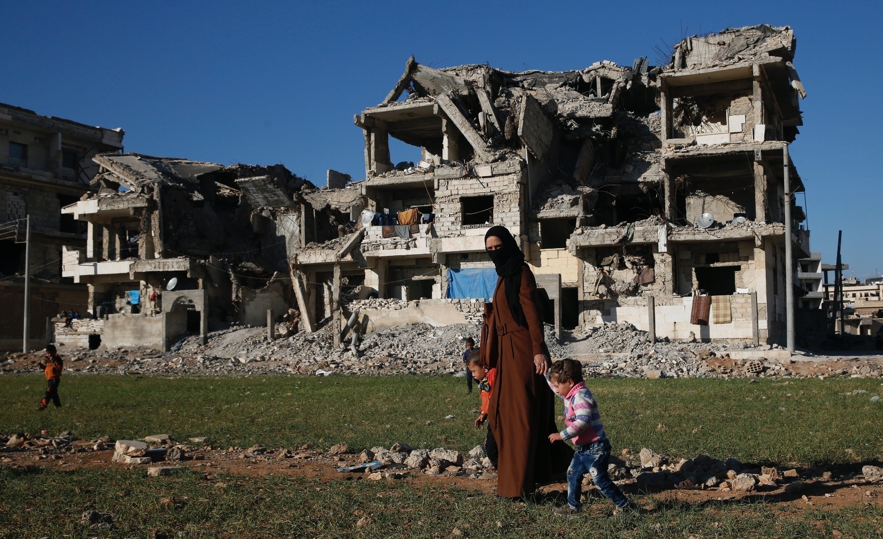 A Syrian woman walks with her kids in front of buildings that were destroyed during clashes between non-state armed groups, Manbij, Syria, March 31.
