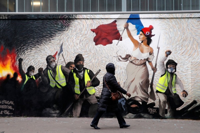A woman passes by a mural by street artist PBOY depicting Yellow Vest (gilets jaunes) protestors inspired by a painting by Eugene Delacroix, ,La Liberte guidant le Peuple, (Liberty Leading the People), in Paris, Thursday, Jan. 10, 2019. (AP Photo)