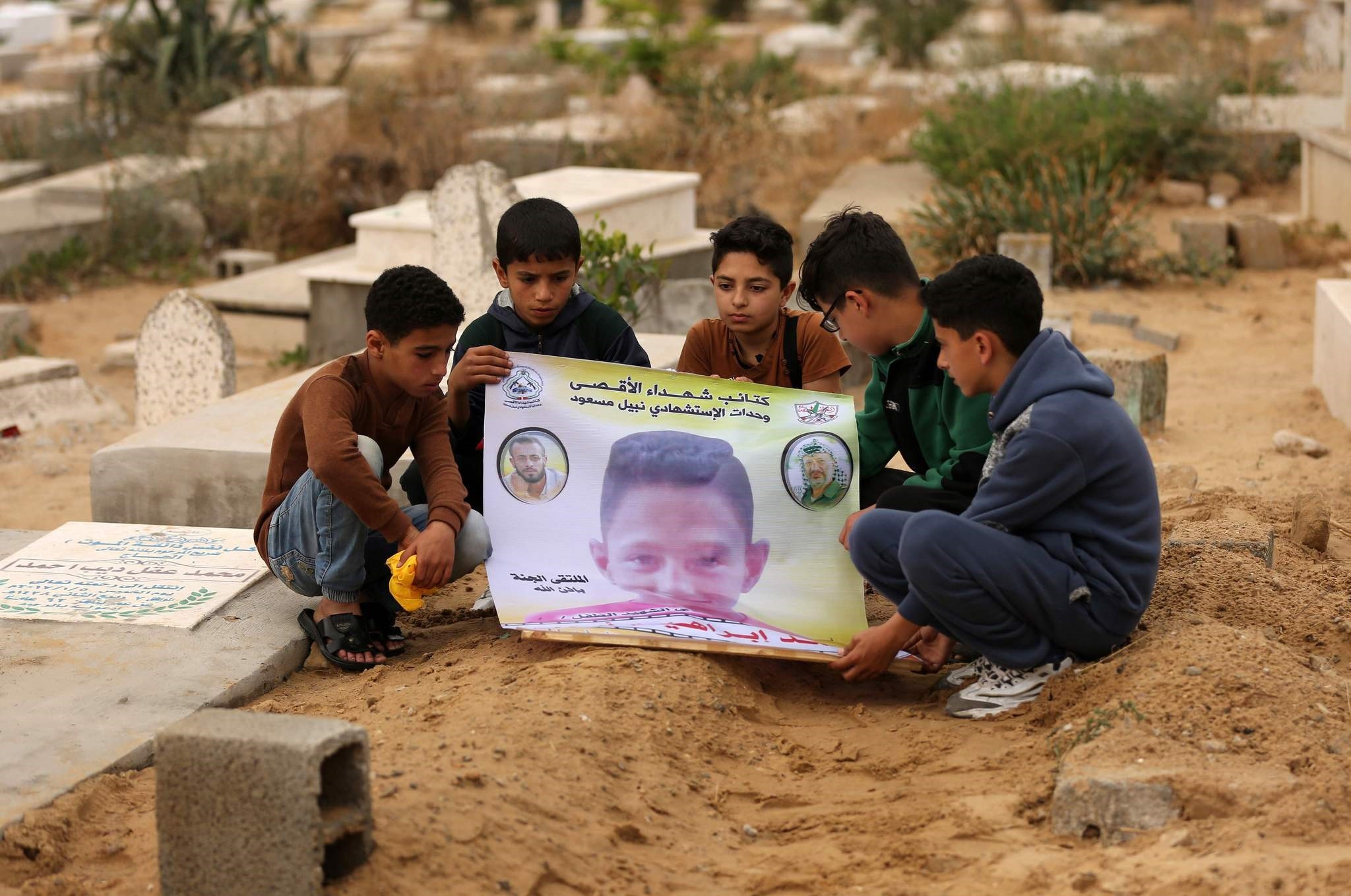 Friends of 15-year-old Palestinian Mohammed Ibrahim Ayoub, who was shot and killed by Israeli security forces during clashes along the Israel-Gaza border, hold up a poster of his portrait by his grave in a cemetery in Gaza. (AFP Photo)