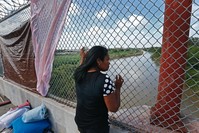 An immigrant from Cuba seeking asylum looks out across the Rio Grande River while waiting on the middle of a bridge to get into the United States from Matamoros, Mexico.