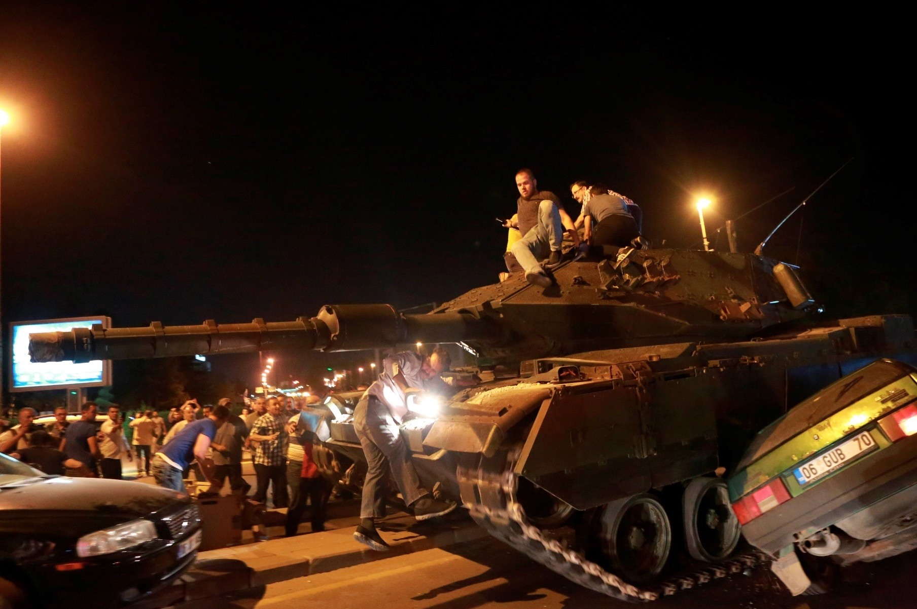 People climb atop a tank occupied by pro-coup troops in Ankara, as it crushes a car, July 15, 2016.