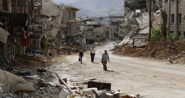 Syrians walk among damaged buildings on a street filled with debris at the mountain resort town of Zabadani in the Damascus countryside, Syria, May 18.