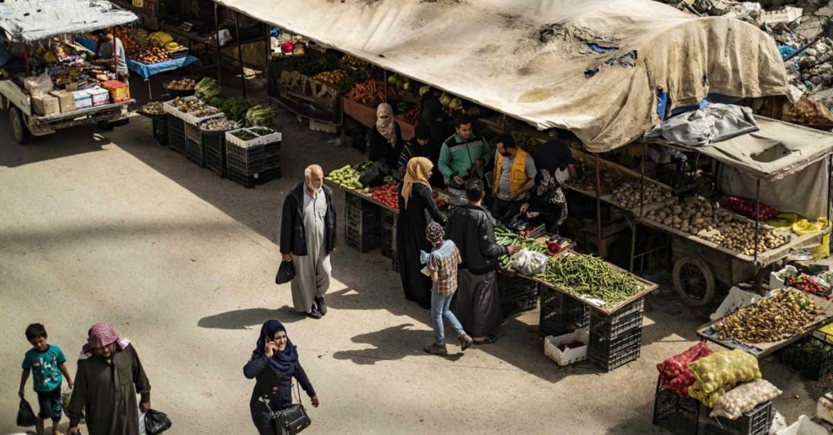 Customers walk near make-shift fruit and vegetable shops set in front of destroyed buildings in the northern Syrian city of Raqa, April 14, 2019. 
