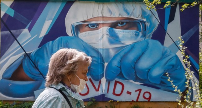 امرأة أمام ملصق إعلاني للتحذير من الفيروس في روسيا EPA