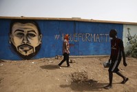 Sudanese artist Asil Diab (L), walks in front of a mural painting of Mohamed Mattar, on the wall of a youth club in Bahri in Khartoum, July 21. Mattar was among dozens killed in the June 3 raid on a protest camp outside the military headquarters.