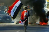 A demonstrator carries an Iraqi flag as he walks near burning tires during ongoing anti-government protests, Najaf, Jan. 12, 2020. (Reuters Photo)