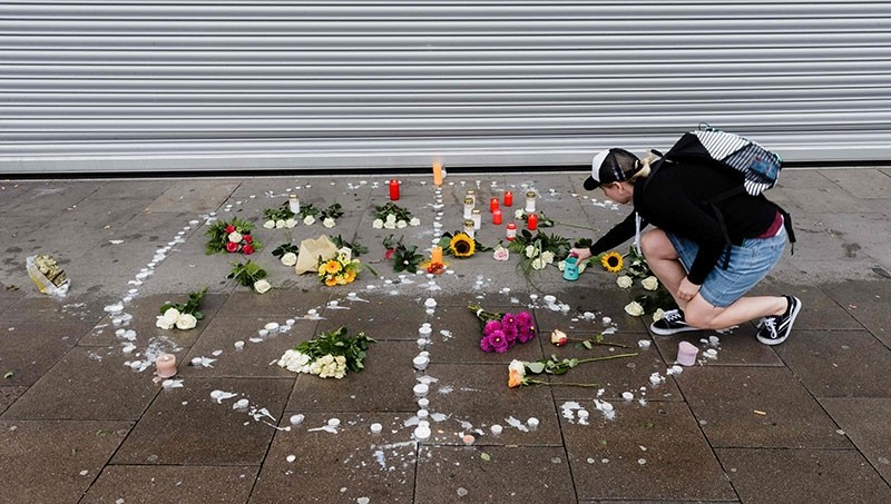 A woman places a candle at a makeshift memorial of flowers and candles arranged like a peace sign on July 29, 2017 in Hamburg, Germany, at the site where a man killed one person and wounded several others in a knife attack the day before. (AFP Photo)