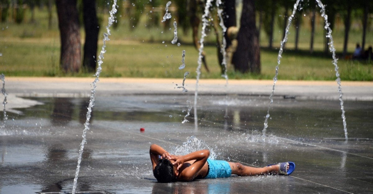 In this file photo taken on June 27, 2019 a boy lies on the pavement as he cools off under water jets at a fountain in Montpellier southern France, during a heat wave. (AFP Photo)