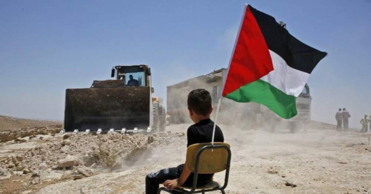 A Palestinian boy sits on a chair with a national flag as Israeli authorities demolish a school site in the village of Yatta, in the occupied West Bank, July 11, 2018. (AFP Photo)