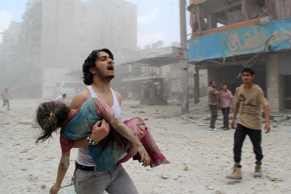 A man carrying a young girl injured in a reported barrel-bomb attack by Assad regime forces in the Kallaseh district in Aleppo, north Syria, June 3, 2014.