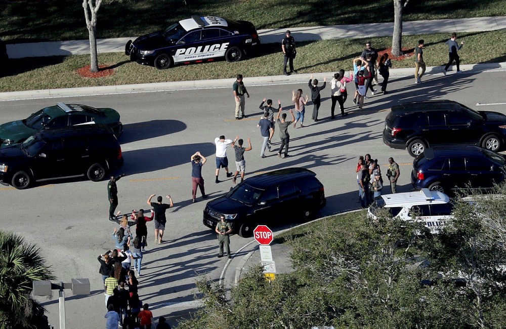 In this Feb. 14, 2018 file photo, students hold their hands in the air as they are evacuated by police from Marjory Stoneman Douglas High School in Parkland, Fla., after a shooter opened fire on the campus. (AP Photo)