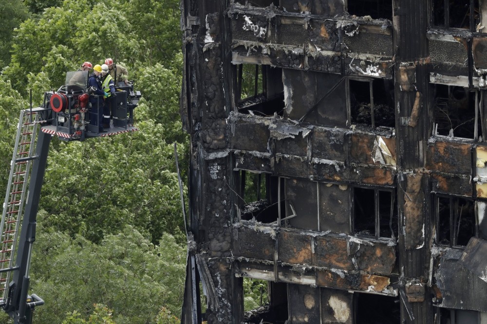 Emergency workers on a raised platform point at a section of the fire-gutted Grenfell Tower in London, Friday, June 16, 2017, after a fire engulfed the 24-story building Wednesday morning.