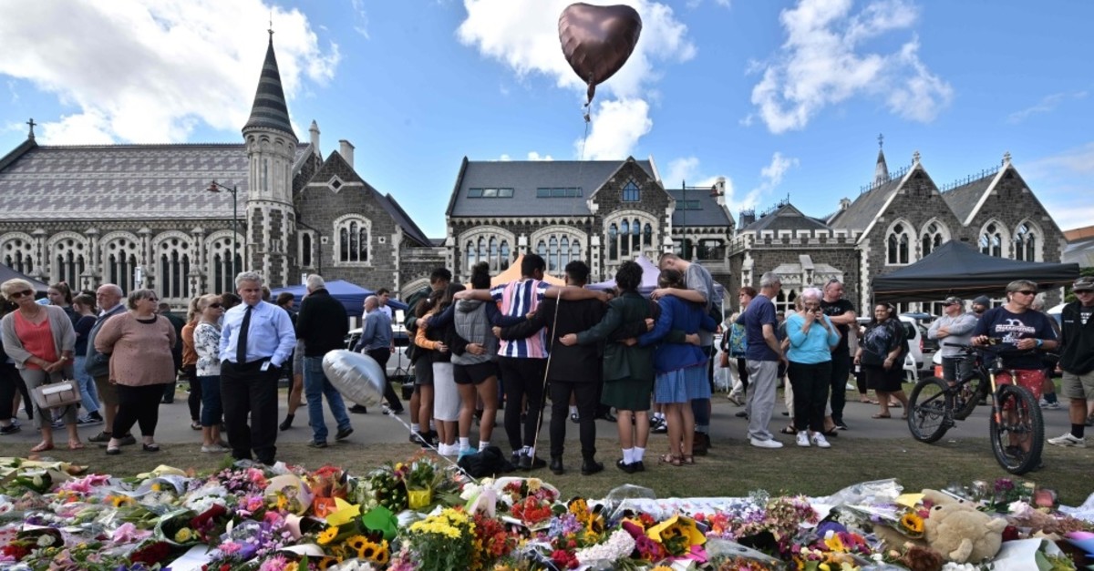 A group of students (C) sings in front of flowers left in tribute to victims at the Botanical Gardens in Christchurch on March 19, 2019, four days after a terrorist attack at two mosques that claimed the lives of 50 people. 