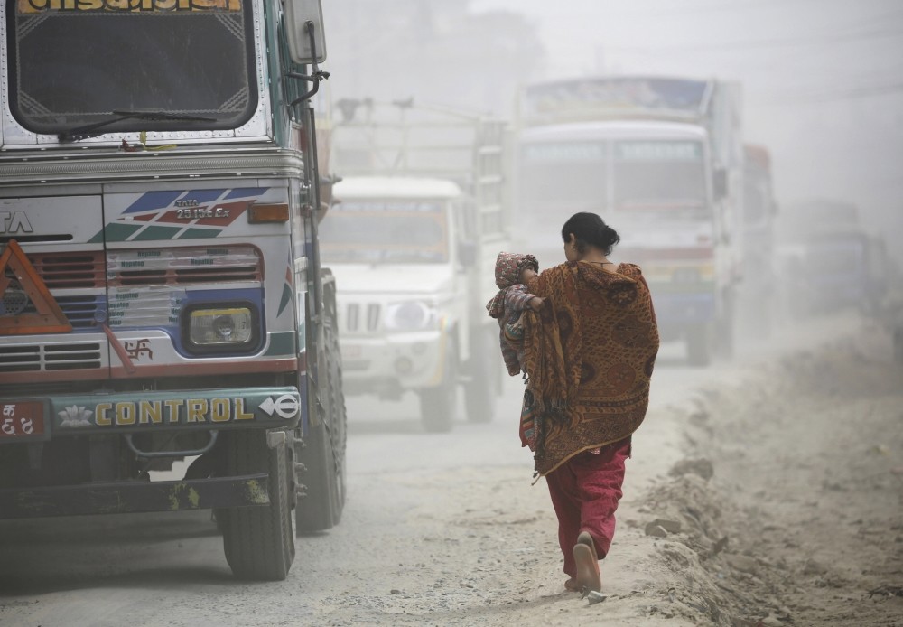A woman carrying her child walks along the dusty road in Kathmandu.