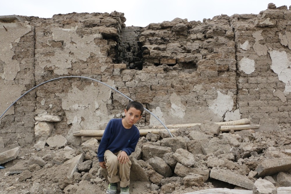 Arda poses in front of his collapsed house.