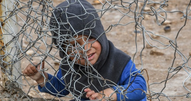 طفل سوري يجلس عند السياج المحيط بمخيم الهول في الحسكة