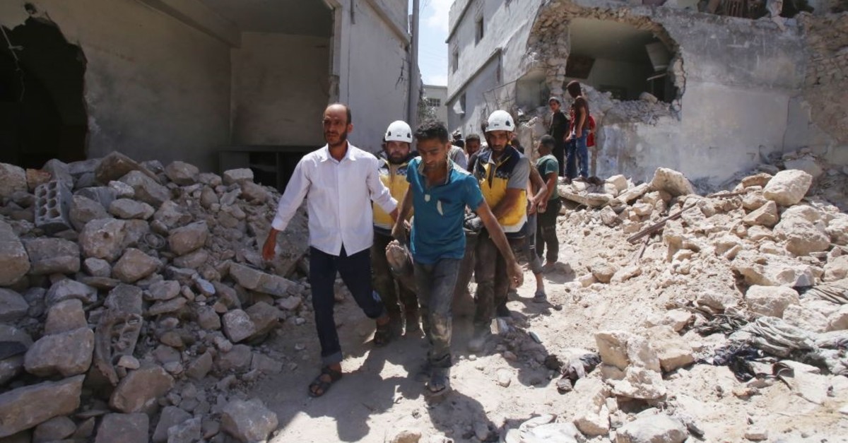 Members of the Syrian Civil Defence (White Helmets) and civilians carry a wounded man following a reported regime airstrike in the southern outskirts of Idlib province, July 12, 2019.