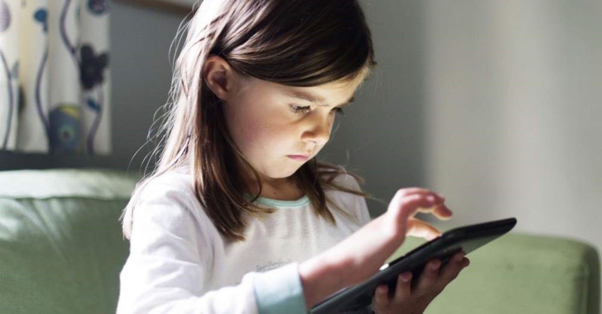 A young girl uses a tablet computer late at night with the glow from the screen on her face. (iStock)