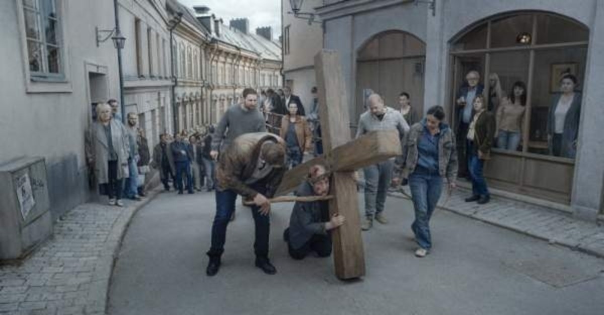 A scene from ,About Endlessness, depicting the priest bearing a huge cross and being tortured by passersby.