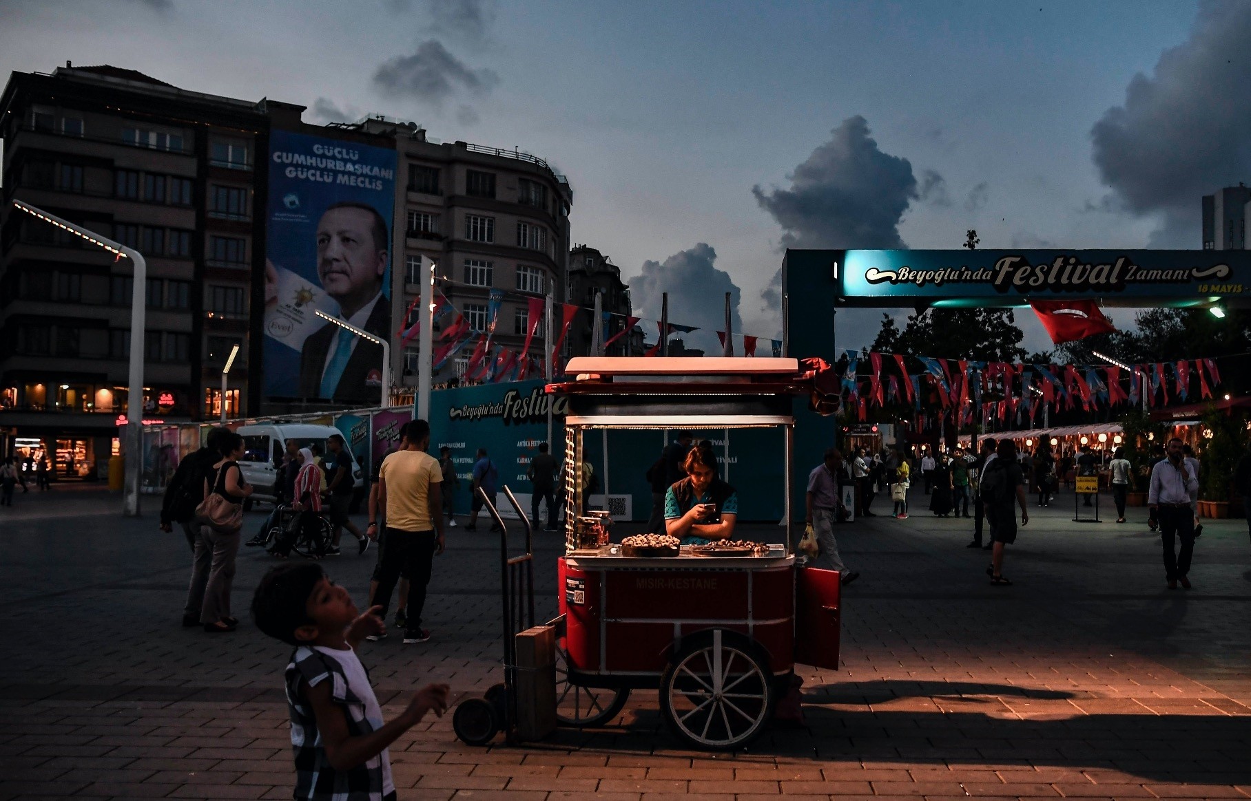 A man sells chestnuts in Taksim Square as a campaign poster for President Recep Tayyip Erdou011fan for the June 24, 2018 elections waves in the background, Istanbul, June 18, 2018.