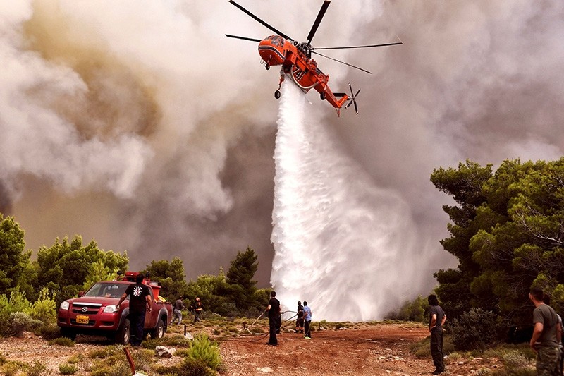 A firefighting helicopter drops water to extinguish flames during a wildfire at the village of Kineta, near Athens, on July 24, 2018. 