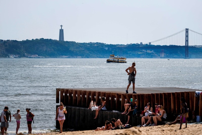 Tourists rest in the shade and cool off on a beach next to Tagus River at Ribeira das Naus in Lisbon on August 3, 2018. (AFP Photo)