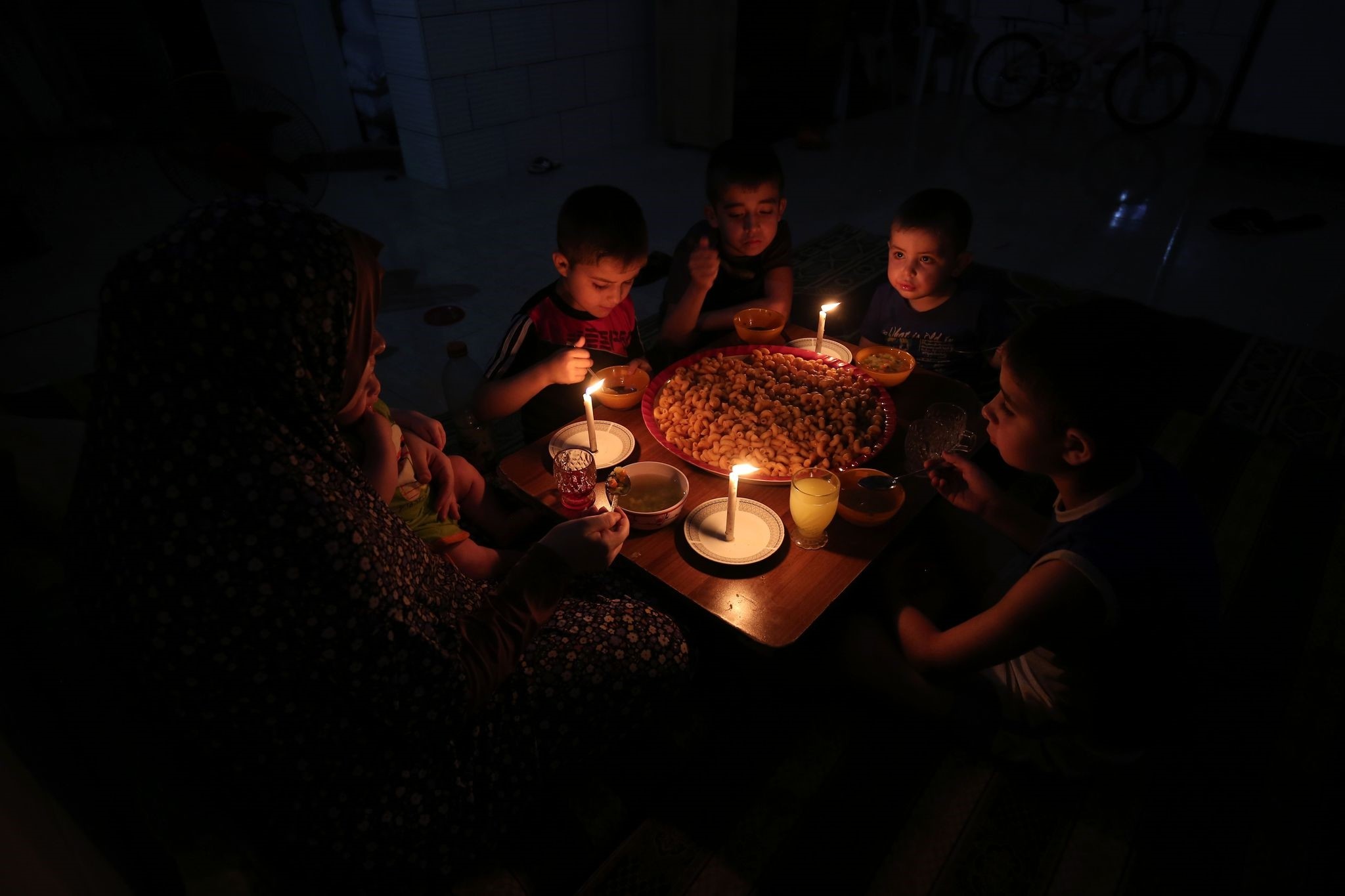 A palestinian family eats dinner by candlelight at their makeshift home in the Rafah refugee camp, in the southern Gaza Strip, during a power outage on June 11, 2017. (AFP PHOTO)