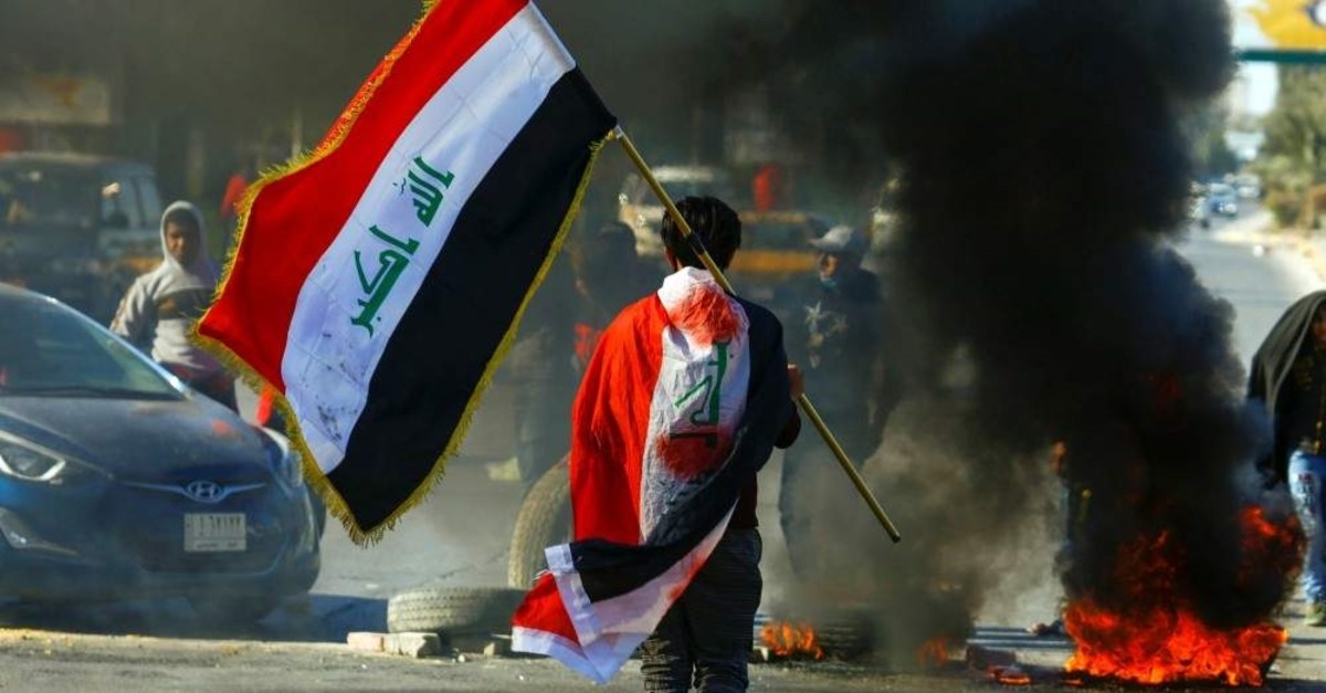 A demonstrator carries an Iraqi flag as he walks near burning tires during ongoing anti-government protests, Najaf, Jan. 12, 2020. (Reuters Photo)